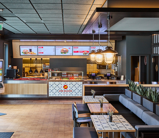 Jim Block Othmarschen Innenansicht Innenansicht des Jim Block Restaurants in Othmarschen mit modernen Sitzbereichen und digitaler Menütafel über dem Bestellcounter.