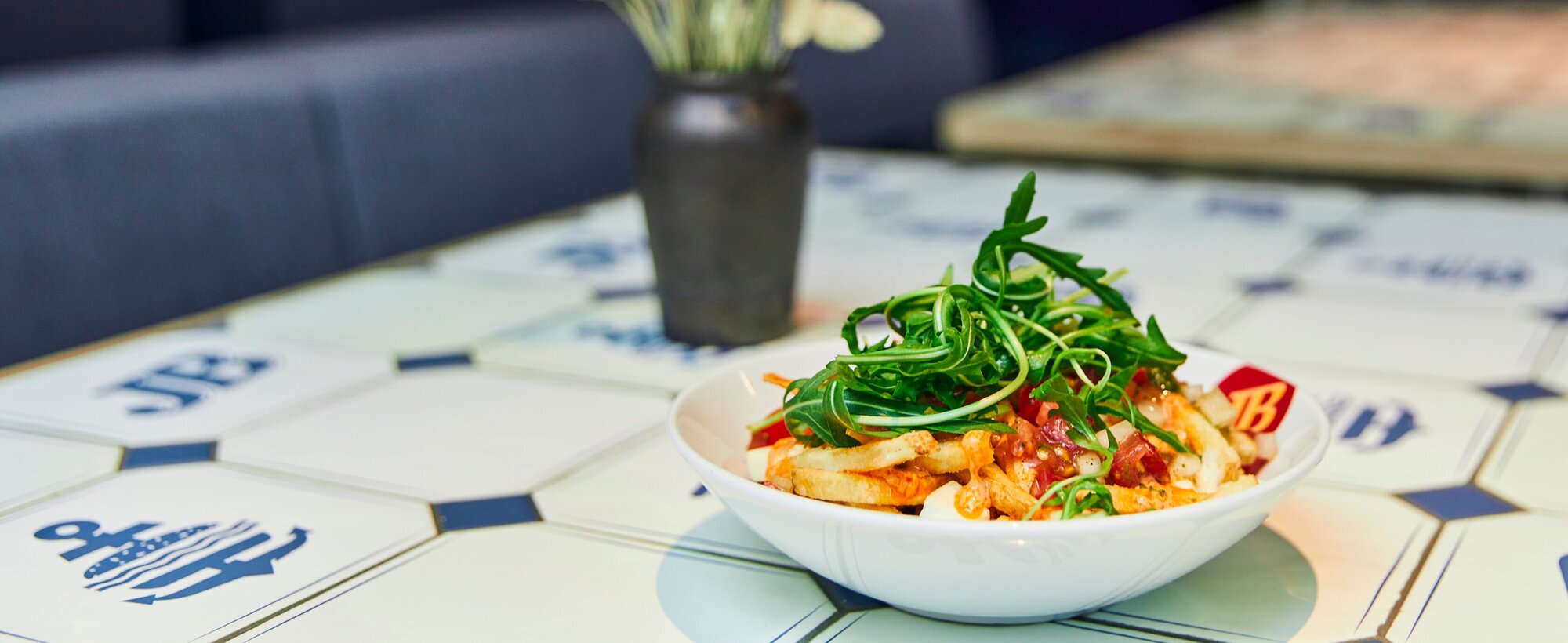 Jim Block Loaded Fries Italian Loaded Fries Italian mit Grana Padano, Tomatensalsa, Rucola und Madurai Sauce in einer weißen Bowl auf JB-Fliesentisch.