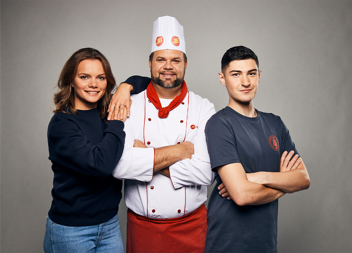 Jim Block Karriere Teamfoto Drei Jim Block Mitarbeitende posieren lächelnd: eine junge Frau im blauen Pullover, ein Koch in weißer Uniform mit rotem Halstuch und ein junger Mann im dunkelblauen T-Shirt