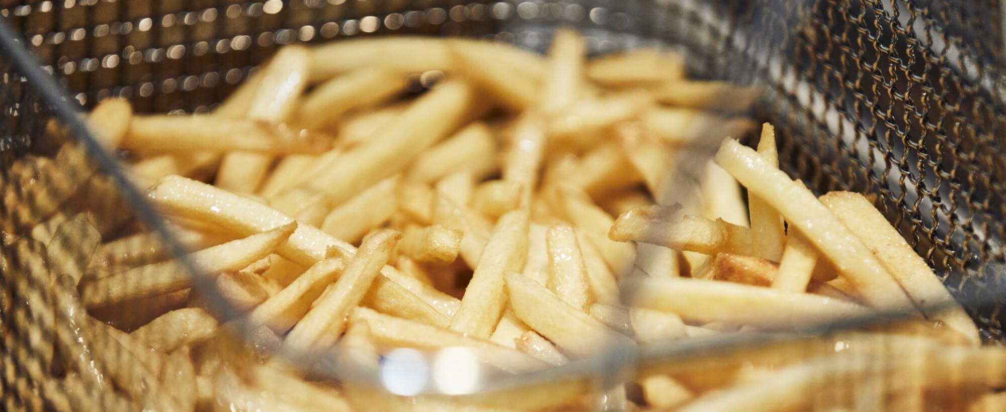 Pommes Frites frisch aus der Fritteuse Frisch frittierte Pommes in einem Frittierkorb.